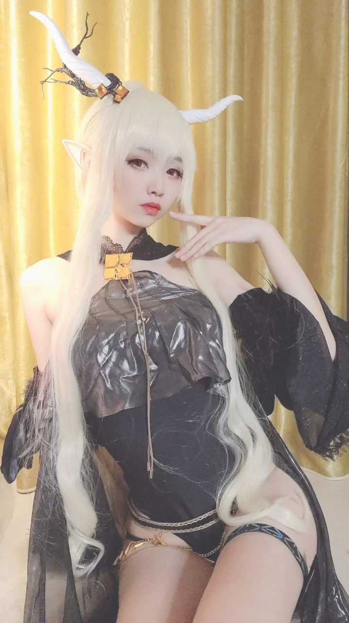 大大卷卷小卷扮演暗色精灵角色，佩戴长白色假发与鹿角配饰，黑色服装带金色装饰，手指轻触下巴