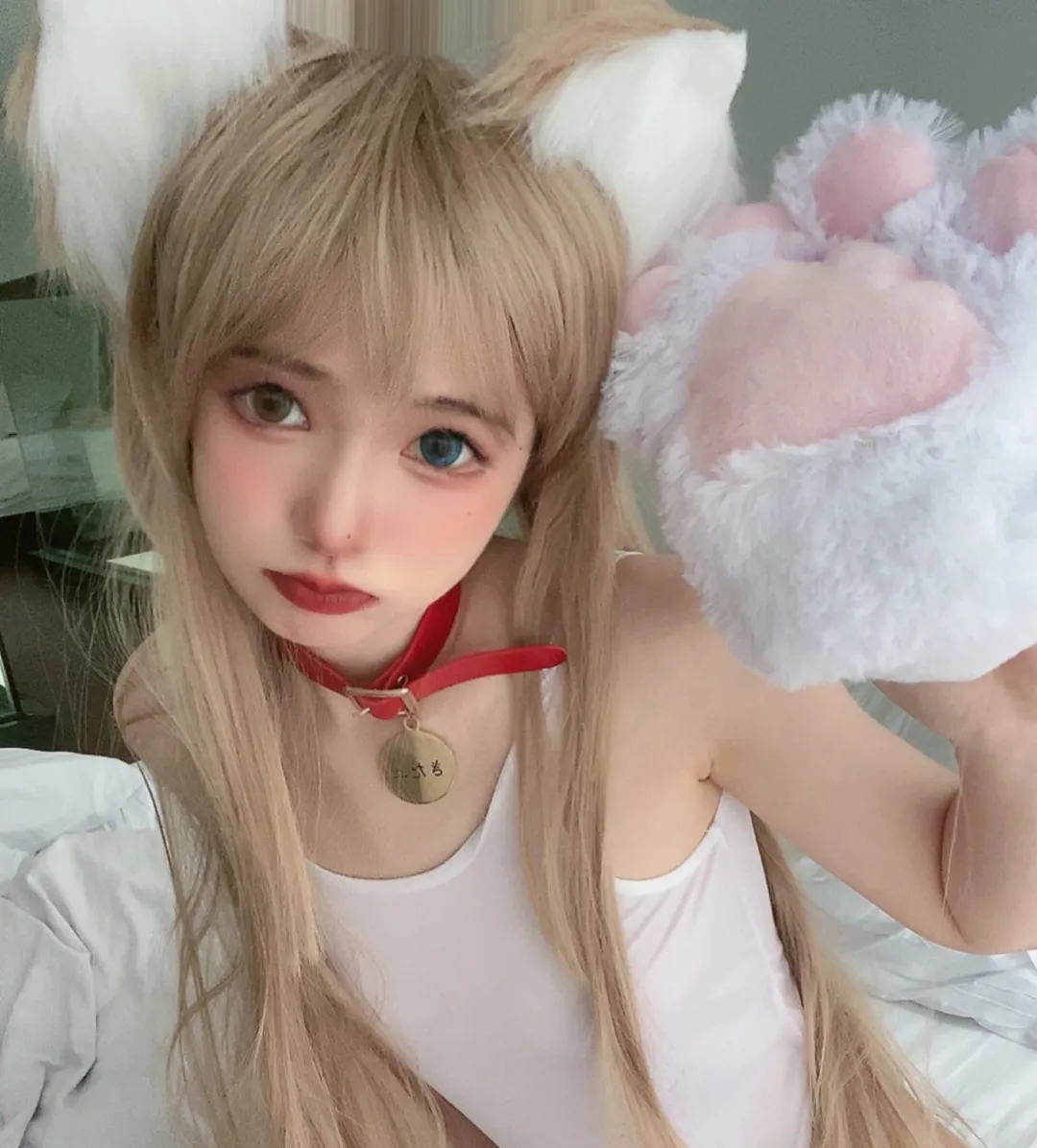 倦倦喵金色双马尾佩戴白色猫耳与红色项圈，举起毛绒猫爪手套靠近镜头，背景为床铺与绿色沙发