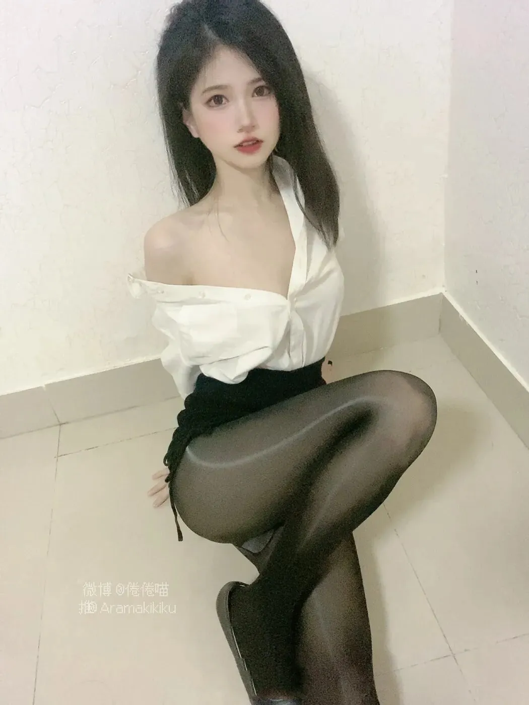 倦倦喵身穿白色衬衫与黑色包臀裙搭配黑色连裤袜，坐在墙角地面低机位拍摄