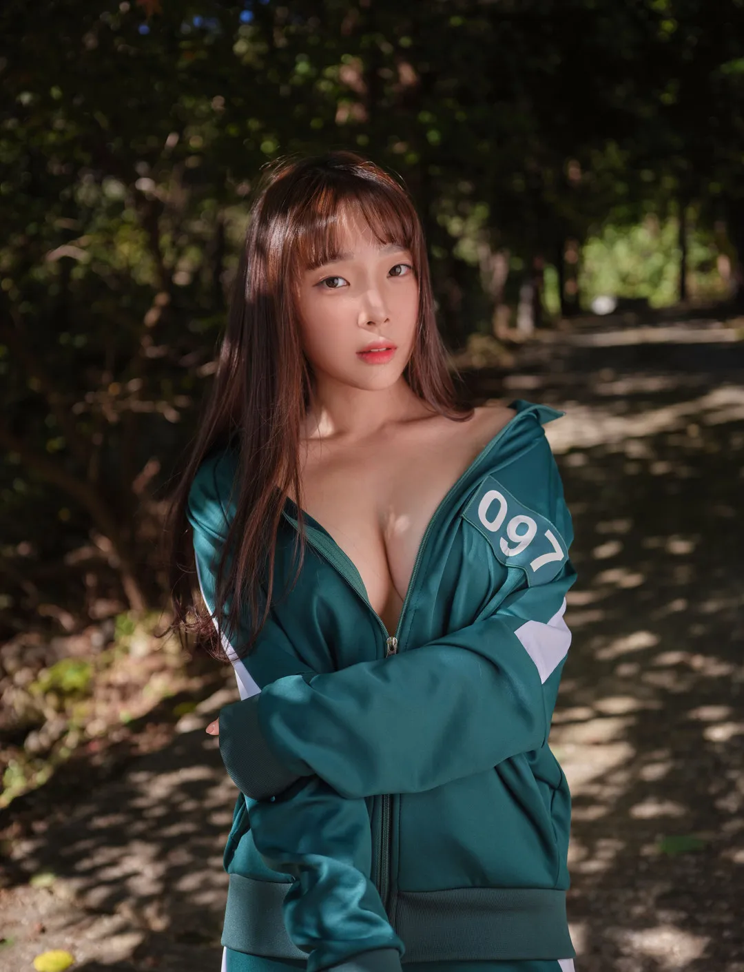 姜仁卿绿色运动外套拉链半开露肩与胸前线条,林间小路斑驳日光下的近景人像