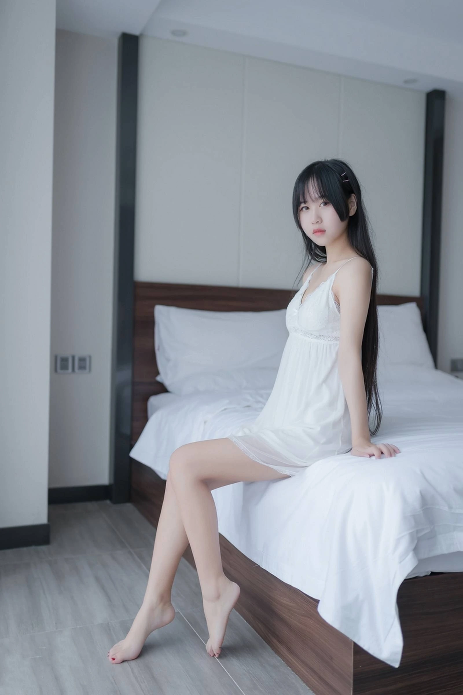 萌芽儿o0在卧室床边穿白色吊带睡裙坐着的照片