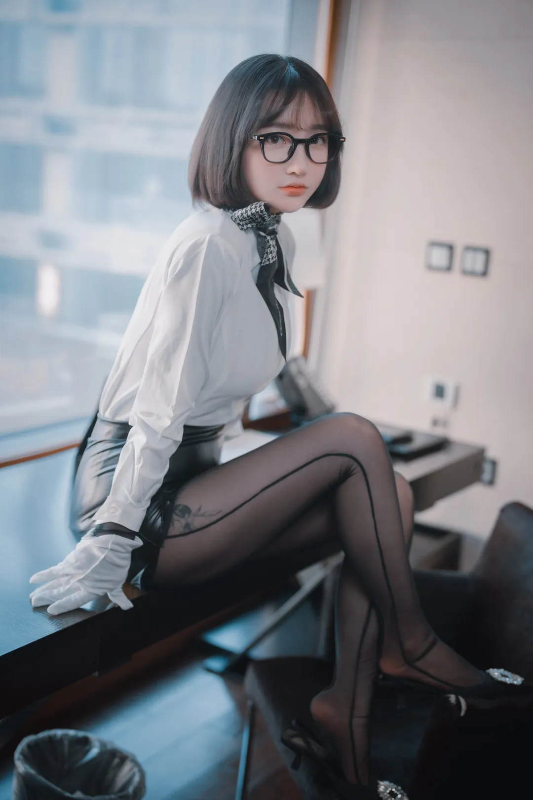 孫樂樂短发波波头戴黑框眼镜,白衬衫系小领巾黑皮裙,黑丝与白手套坐在桌边,窗外城市虚化背景