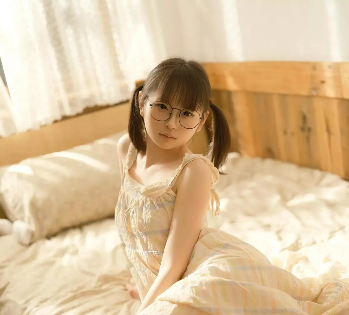 幼水铃衣在床上戴眼镜穿浅色吊带睡裙坐着的照片