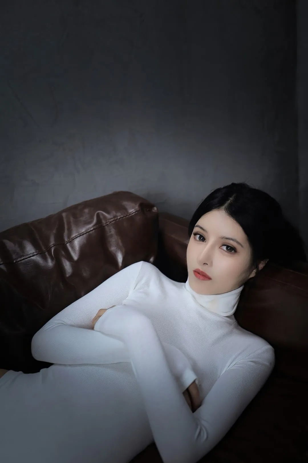 抖叔穿白色高领坐在深色沙发上，交叠手臂和暗调光线突出气质