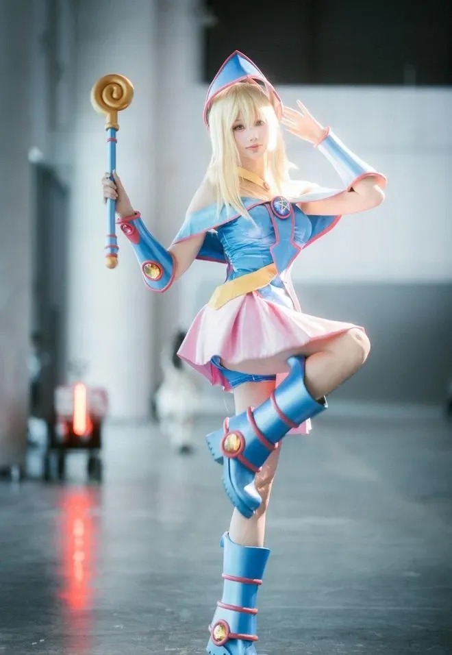 黄金二逼王在展馆空间中穿蓝粉魔法少女服,单腿站立并举起法杖的COS造型