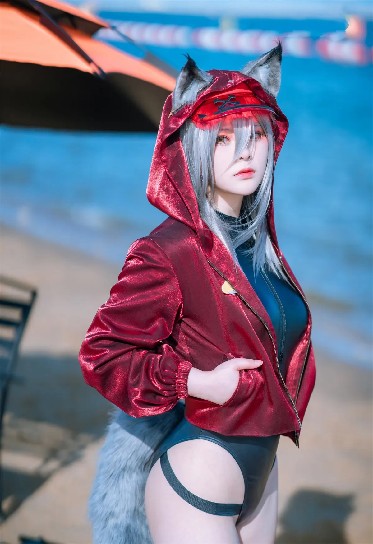w百合欧皇子w cosplay 银发狼耳角色，海滩边侧身站立，穿红色光泽连帽夹克与深色连体泳衣
