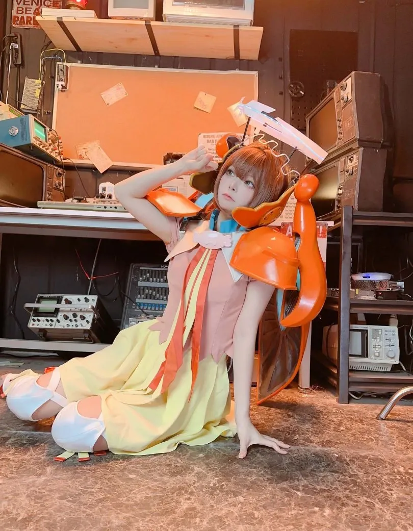 w百合欧皇子w cosplay 橙色机甲 cosplay 服装,坐姿于复古电子设备堆砌的暗色场景中,右手抬至头部旁侧