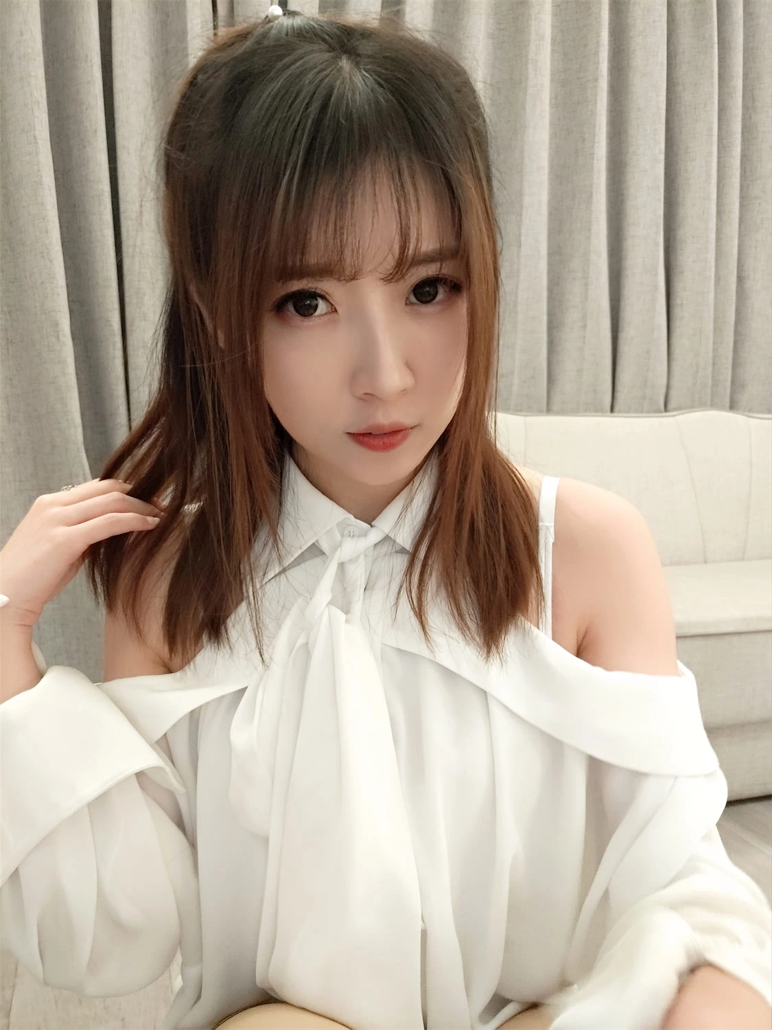 小女巫露娜在浅色窗帘前白色露肩上衣近景坐姿出镜,发型与领口细节清晰