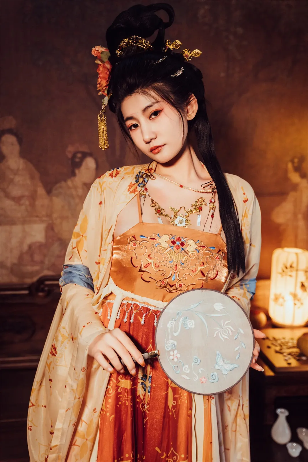 星澜是澜澜叫澜妹呀古风长裙半身实拍,盘发配金色发饰,手持团扇站在暖色室内