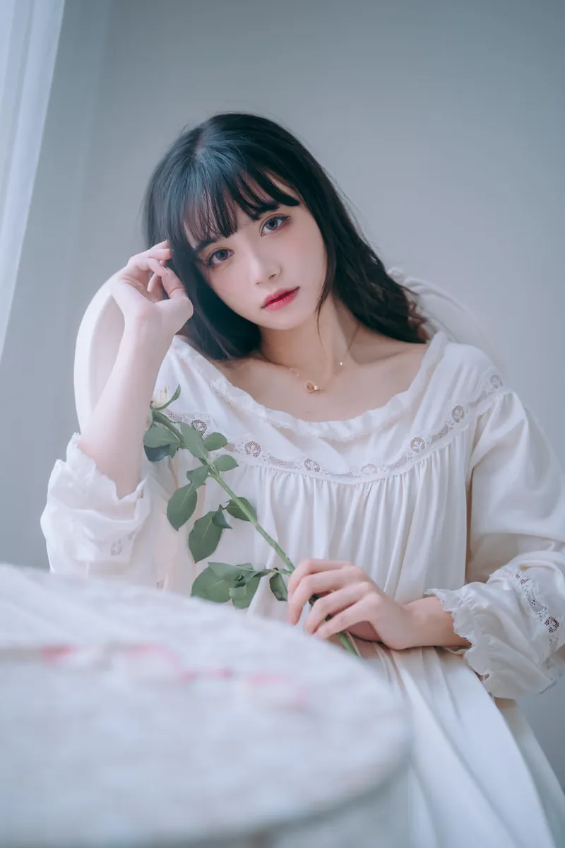 Joyce 黑色长发白色连衣裙室内写真，手持绿色枝叶坐在浅色背景前