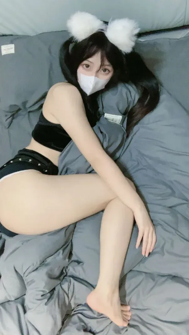 突变的柠檬黑色居家服造型,佩戴白色毛绒发饰和白色口罩,侧躺在灰色床品上