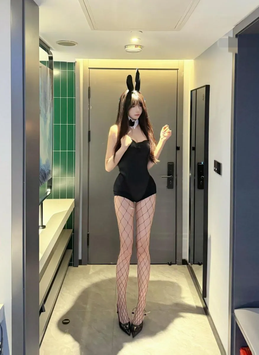 抖音神明同同长发戴黑色兔耳发箍,穿黑色连体服站在室内走廊