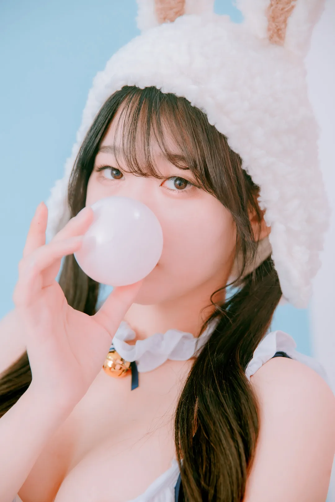 Zia(지아)戴白色兔耳帽吹泡泡糖在蓝色背景前拍摄写真