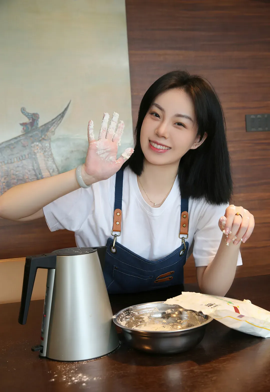 一颗甜蛋黄a黑色短发微笑，穿白色T恤和蓝色围裙在桌前举起沾粉手掌