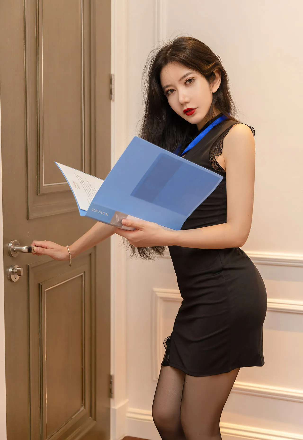 心妍小公主穿黑色连衣裙拿蓝色文件夹站在门边的写真